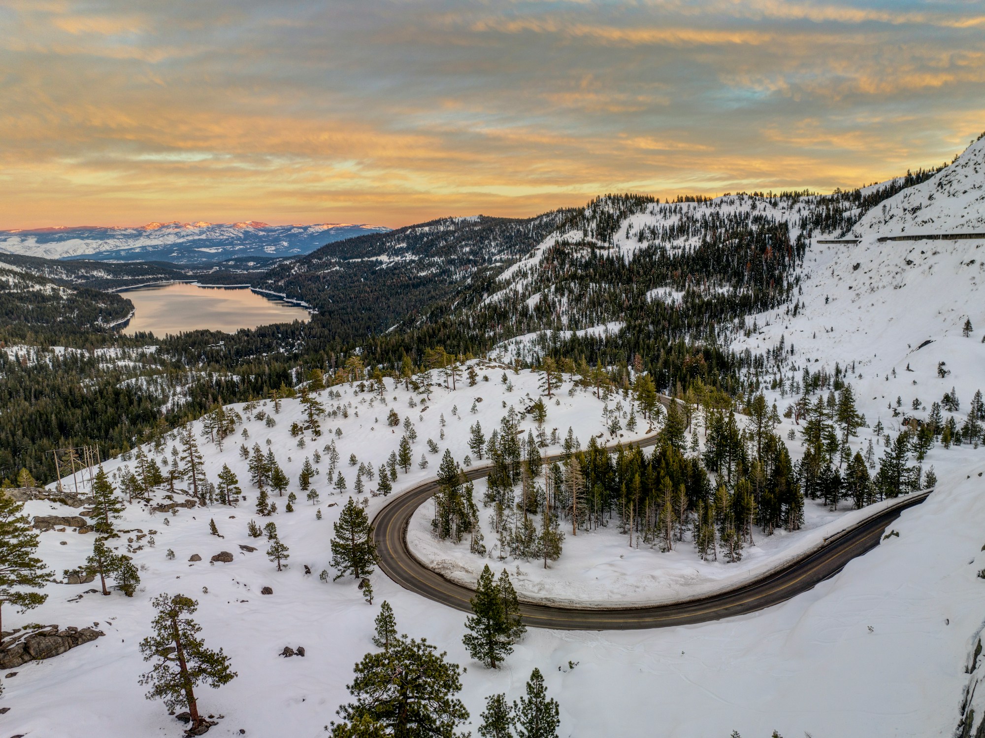 A winding mountain road through snow-dusted peaks at sunset — the road ahead